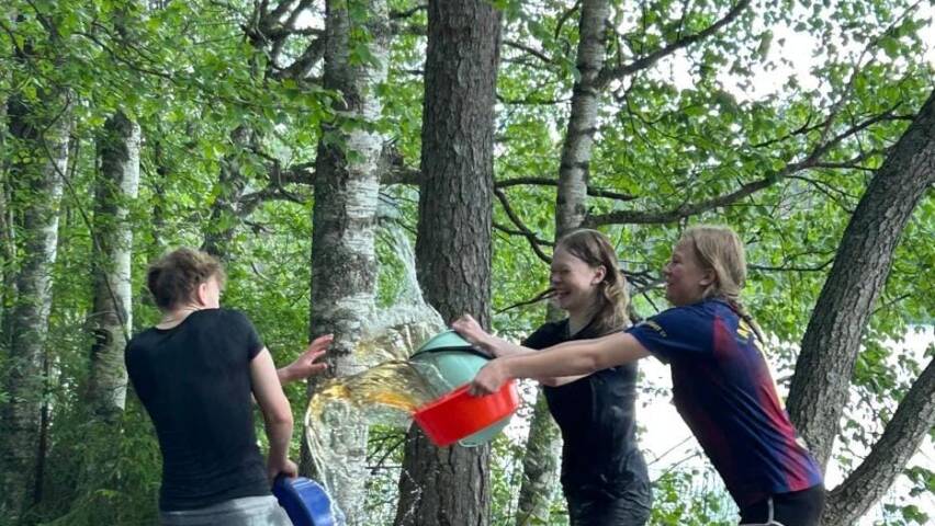 Kolme nuorta rippileirillä leikkimässä vesisotaa lammen rannalla.