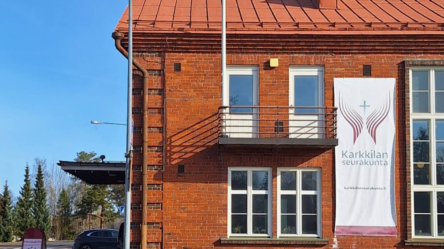 Pohjanpirtin punainen tiilirakennus, parveke, ikkunoita ja Karkkilan seurakunnan logo isossa banderollissa seinällä.