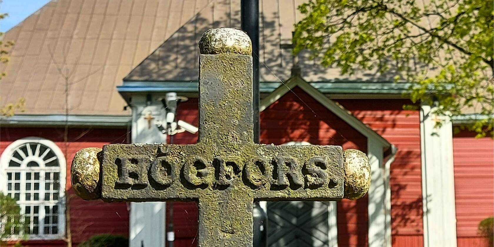 Taustalla Karkkilan kirkko ja etulalalla vanha rautaristi hautausmaalla, jossa lukee Högfors.