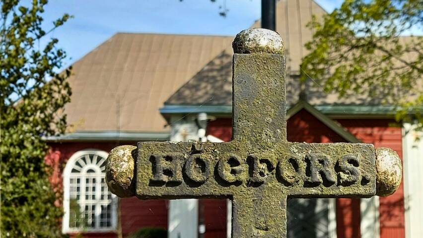 Taustalla Karkkilan kirkko ja etulalalla vanha rautaristi hautausmaalla, jossa lukee Högfors.