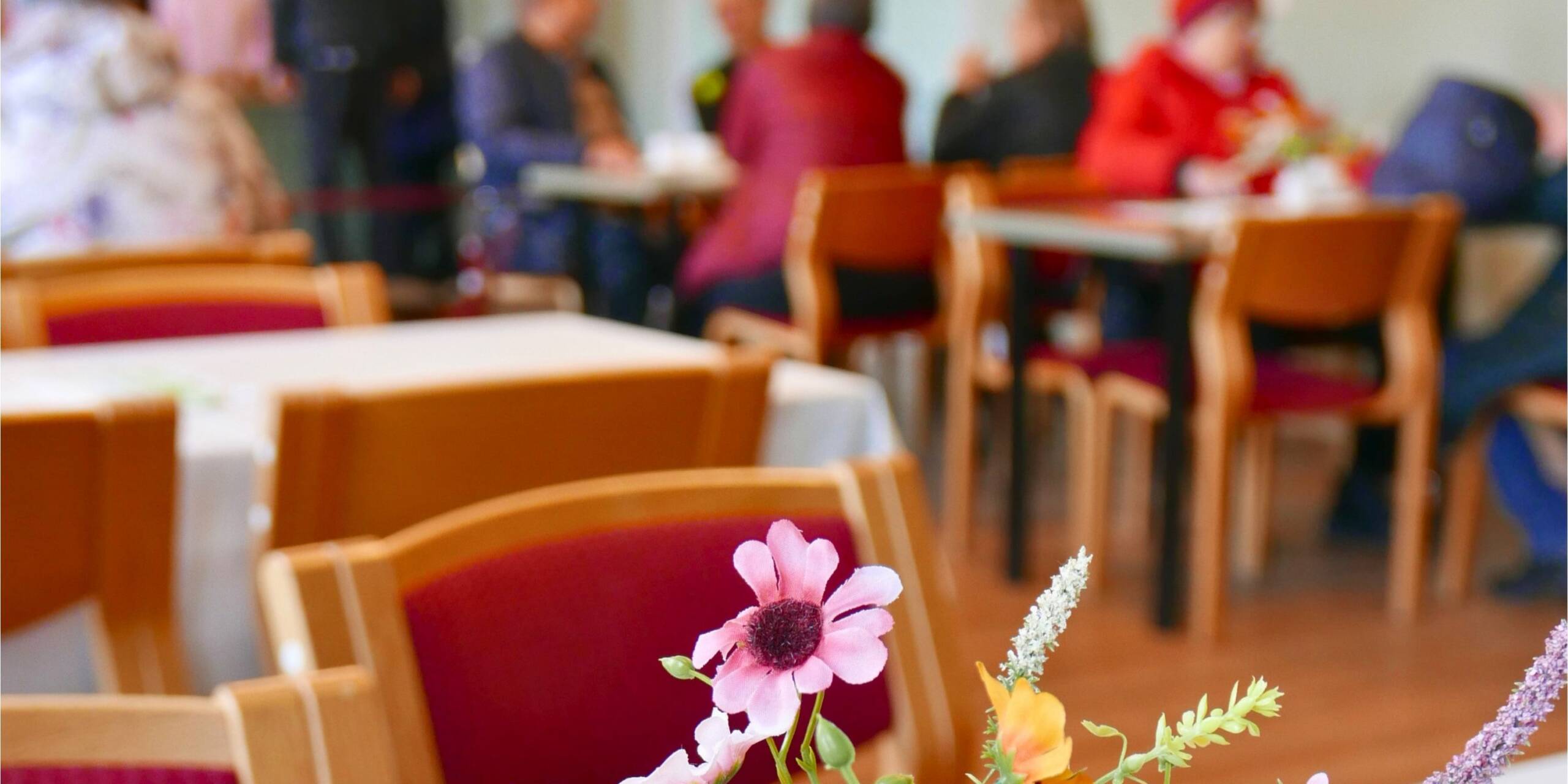 Värikkäitä kukkia pöydällä ja kauempana sumennettuna ihmisiä kahvilapöydissä.