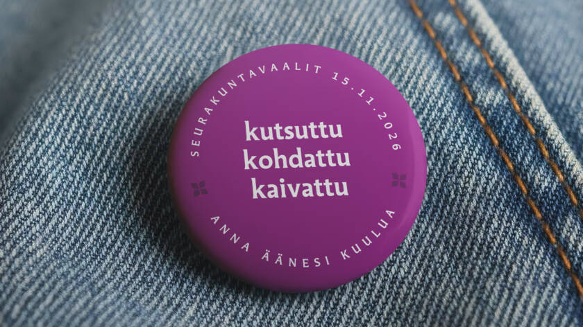 Lähikuva sinisen farkkutakin rintamuksesta, johon on kiinnitetty violetti pinssi tekstillä Kutsuttu, Kohdattu, Kaivattu, Seurakuntavaalit 15.11.2026, Anna äänesi kuulua.