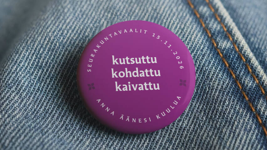 Lähikuva sinisen farkkutakin rintamuksesta, johon on kiinnitetty violetti pinssi tekstillä Kutsuttu, Kohdattu, Kaivattu, Seurakuntavaalit 15.11.2026, Anna äänesi kuulua.