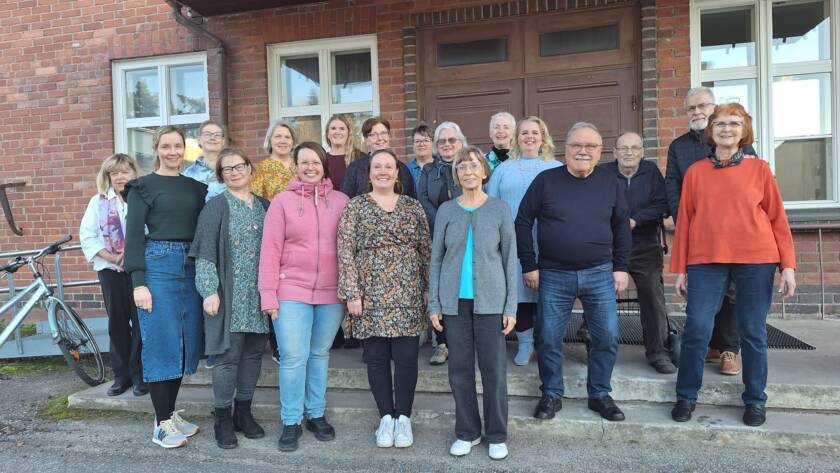 Kirkkokuorolaiset Pohjanpirtin ylko-oven edessä Anne Rahko-Leinon kanssa.